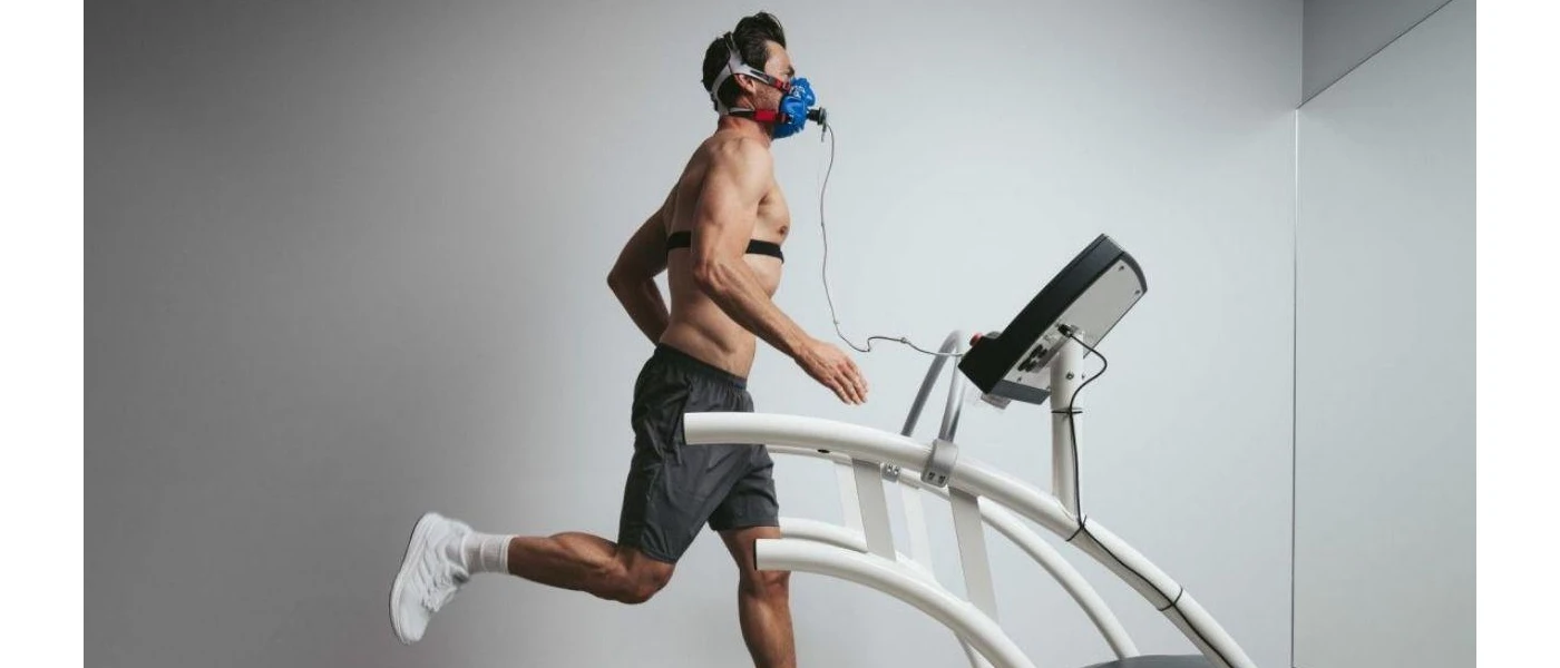 Slim man with dark hair in grey shorts, running on a machine while hooked up to a mask and tubes