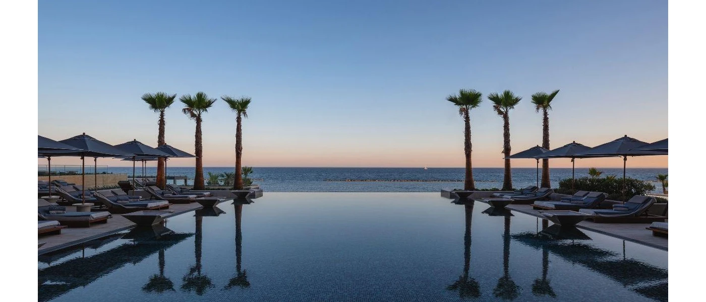 Infinity pool at sunset, with the outline of sun loungers and parasols and tall palm trees at the edge
