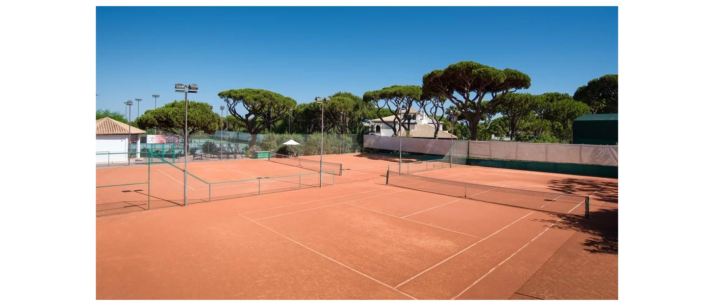 Terracotta-hued tennis courts surrounded by gardens under a blue sky