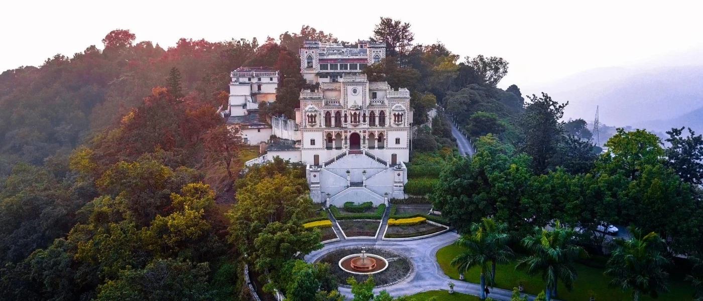 Colonial Indian palace on a hillside among trees and shrubs, with a landscaped roundabout in front