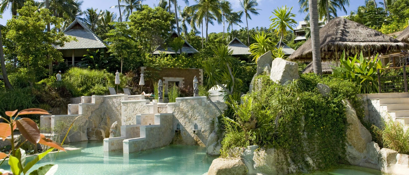 Tropical gardens, stone pathways, steps and parasols framing a grotto-like pool