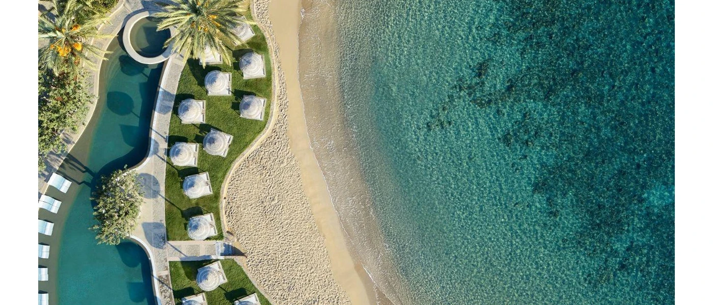 Aerial view of a swimming pool, lawn with loungers and parasols, sandy beach and the sea