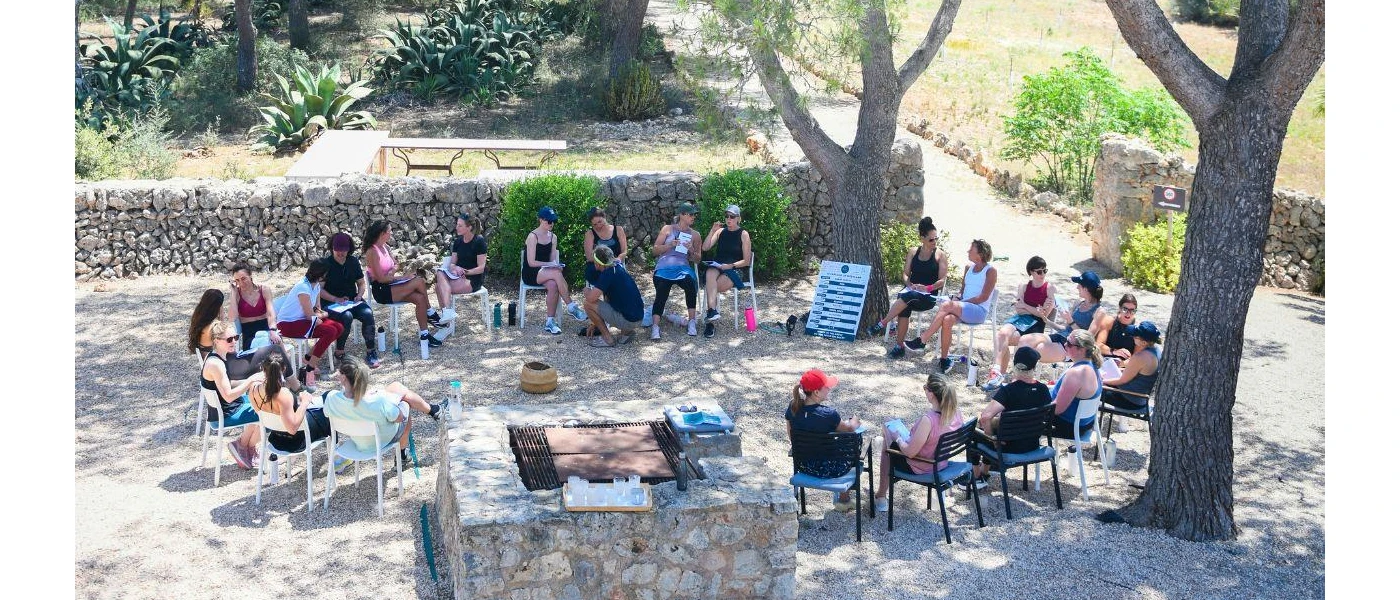 Group sit in chairs in a circle in a stone courtyard surrounded by greenery