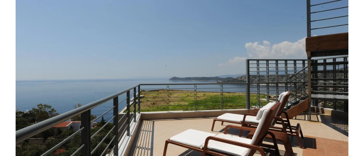 Sea-facing sunny terrace with two ivory-cushioned loungers under a blue sky