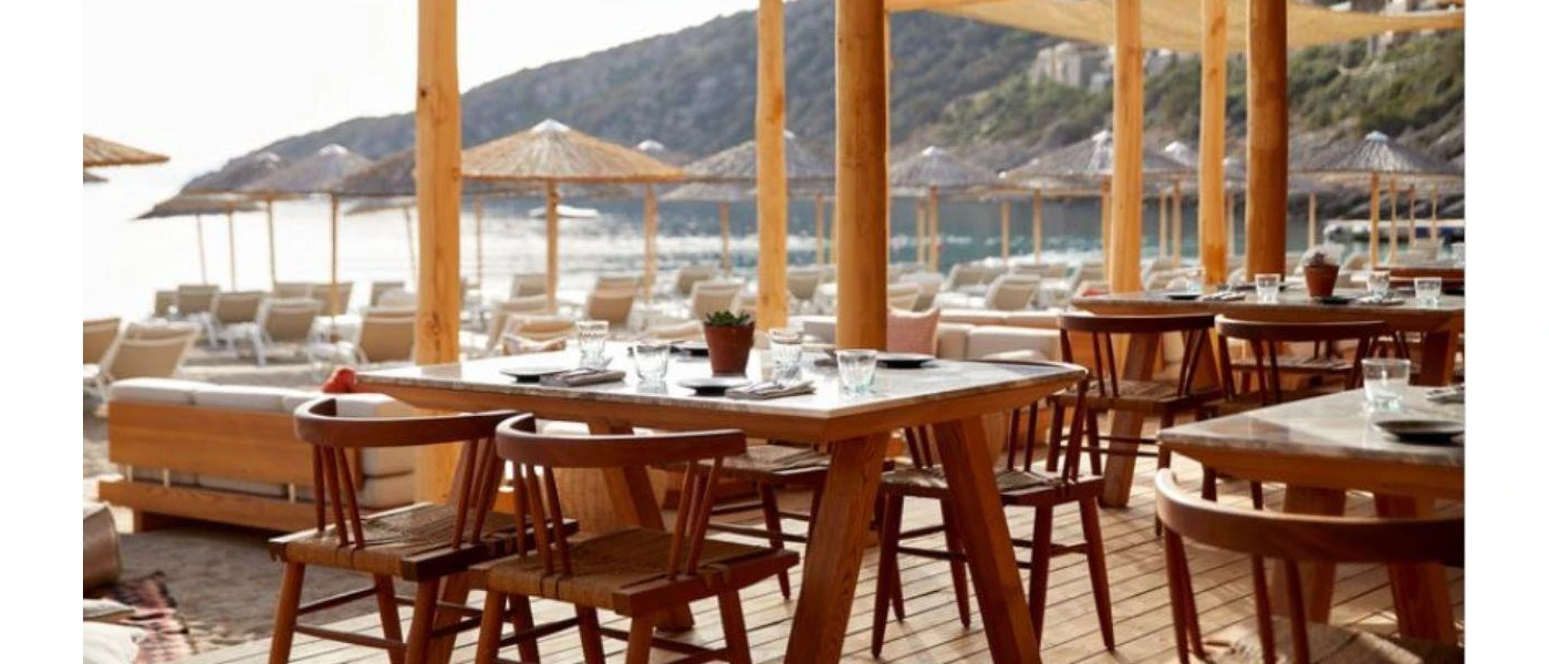 Rustic-chic beach club with wooden flooring and stilts, a terrace with neutral sofas and thatched umbrellas in the background