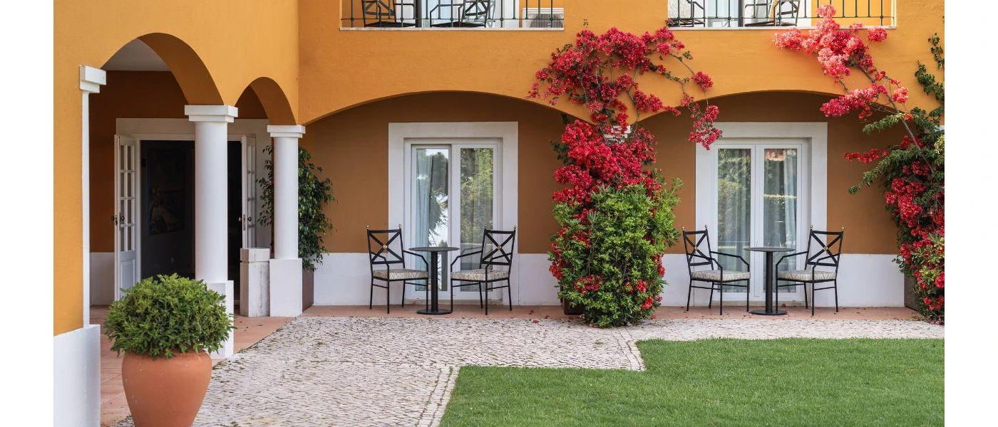 Mustard building with white pillars, pinks blooms and a grassy lawn