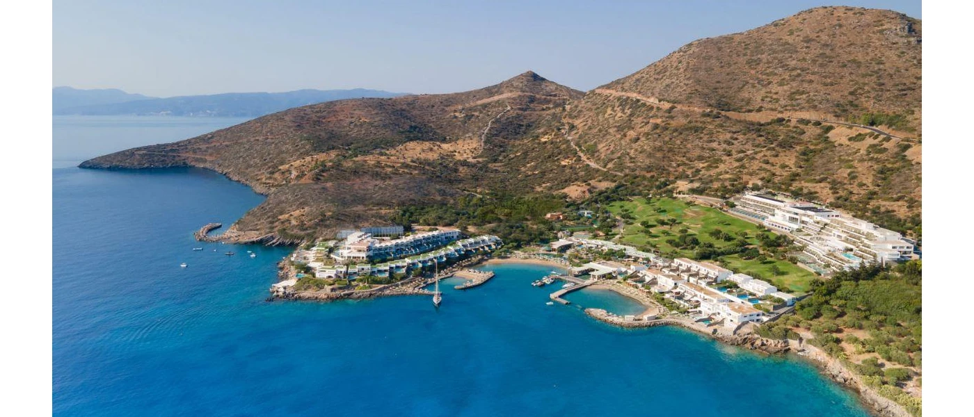 Aerial view of Mirabello Bay, overlooked by a white resort and hills under a blue sky