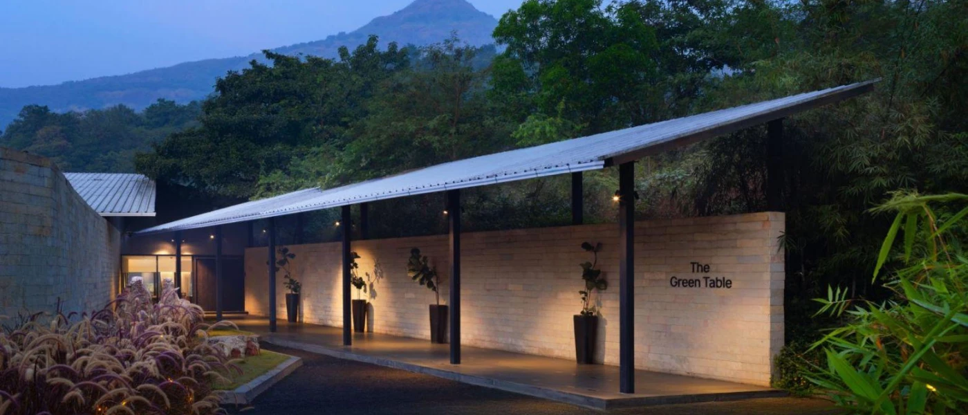 Low canopy roof with the words 'The Green Table' written on the brick wall below, and potted plants lining the entrance