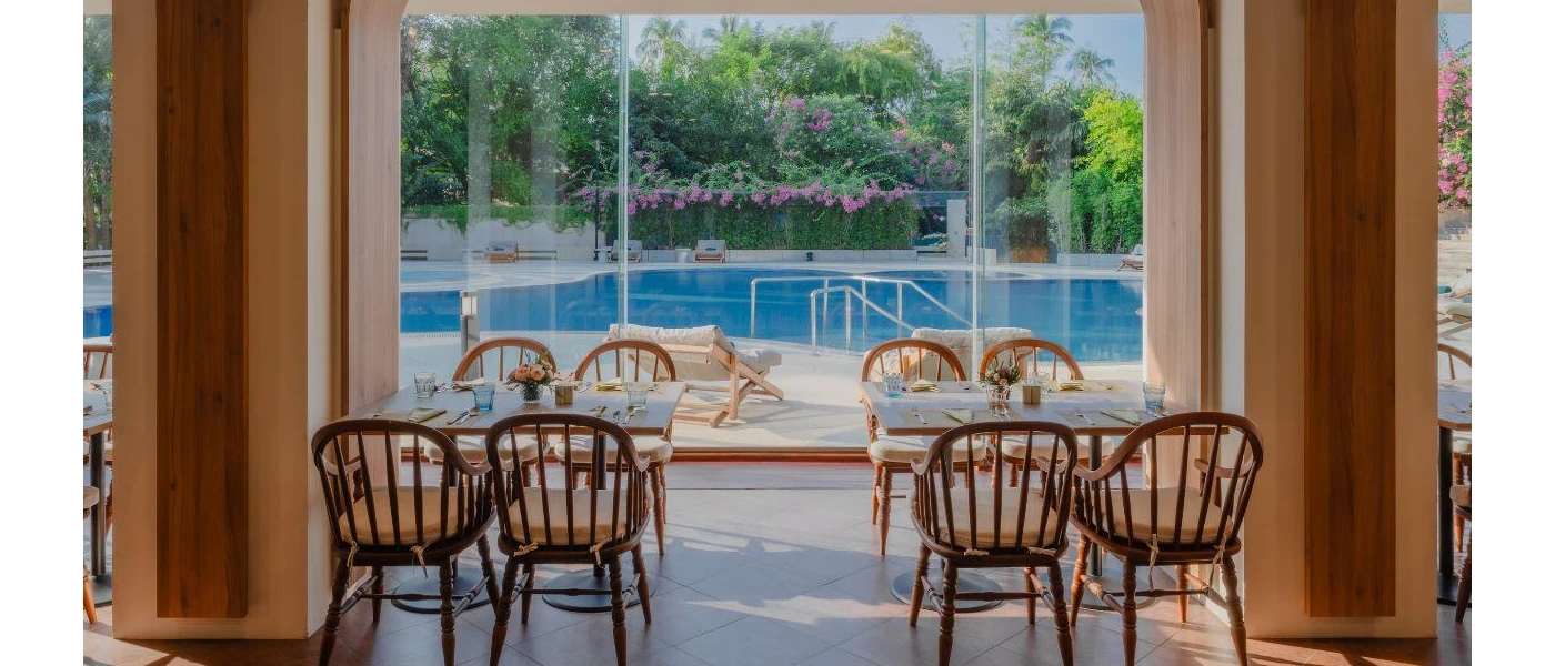 Restaurant with wooden tables and chairs, full-length glass doors and a view of the pool