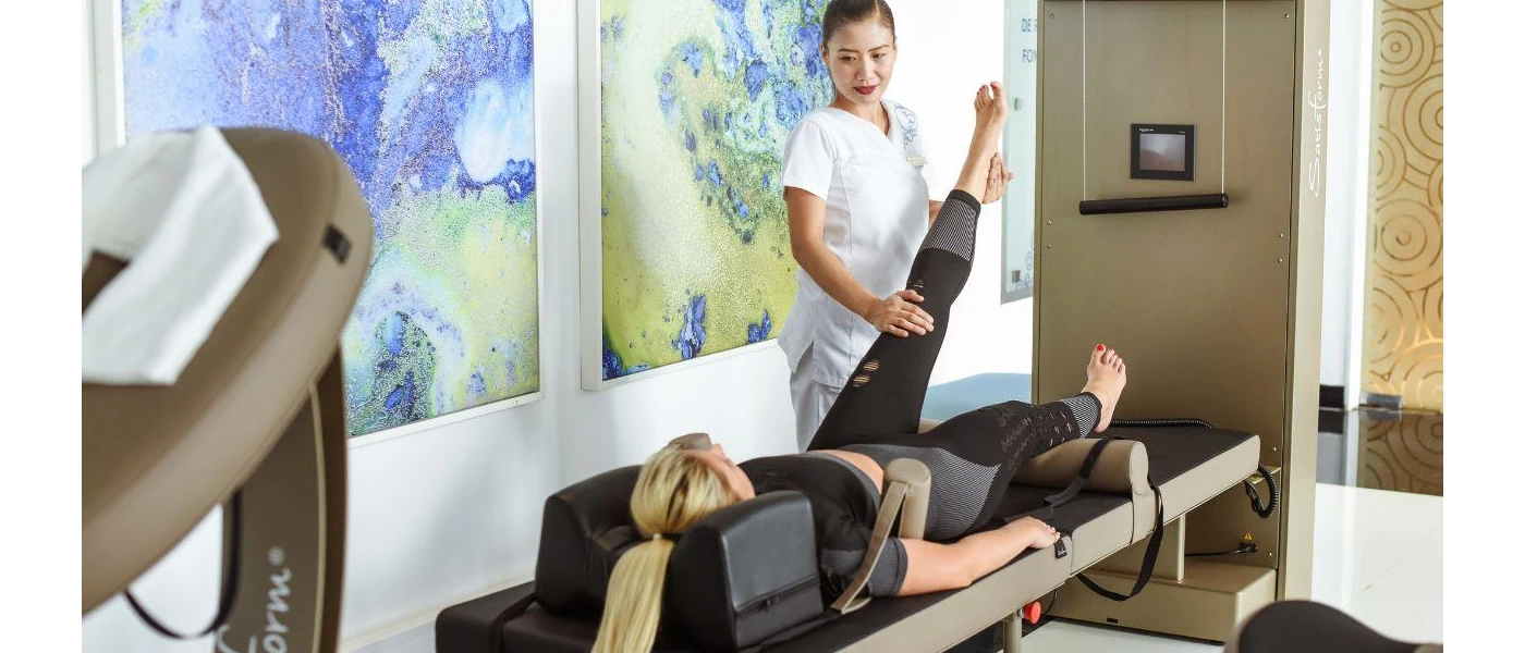 Woman in white uniform holding up the leg of another woman as she lies on a bed surrounded by medical equipment