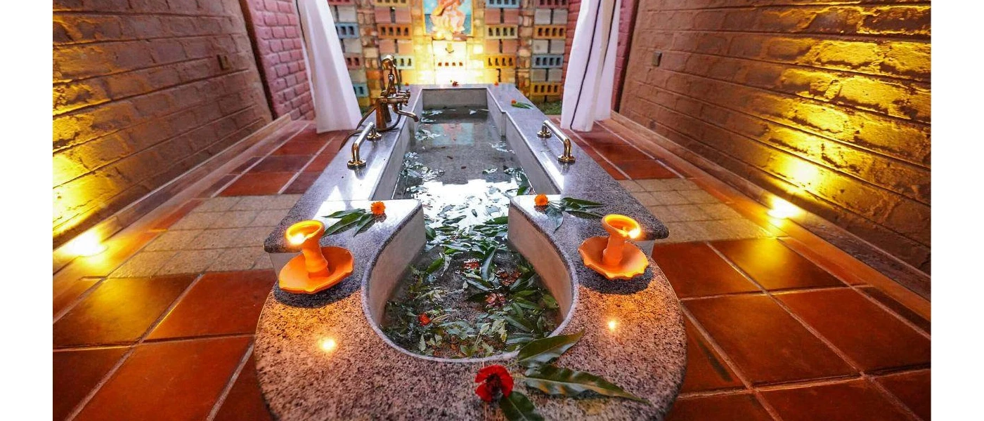 Bath filled with water and leaves in a candelit room with tiled floors and stone walls