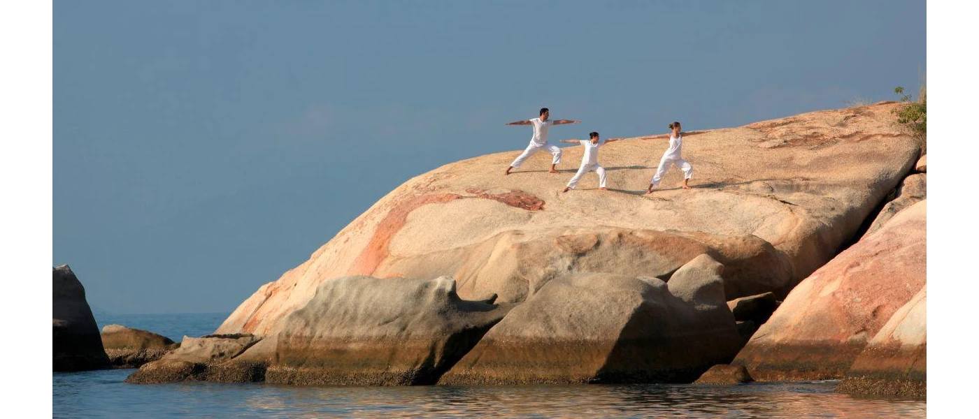 Three people in white in a yoga pose on a rock face on a sunny rock formation