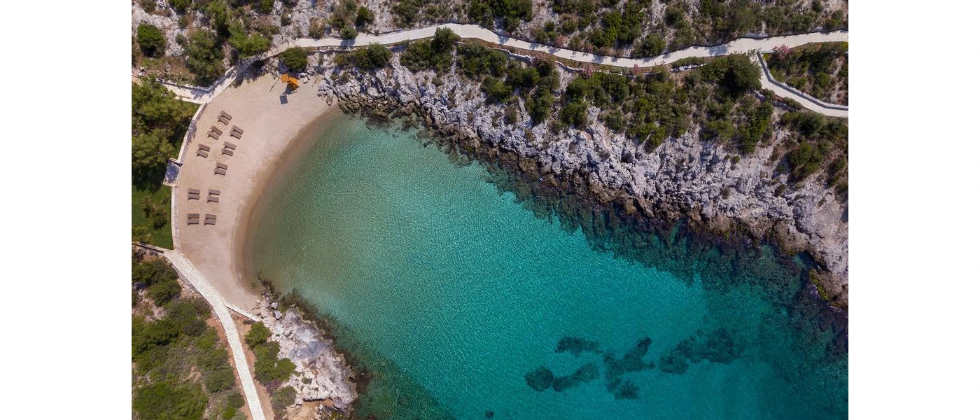 Aerial view of a sandy bay lapped by clear turquoise shallows and surrounded by rocky cliffs