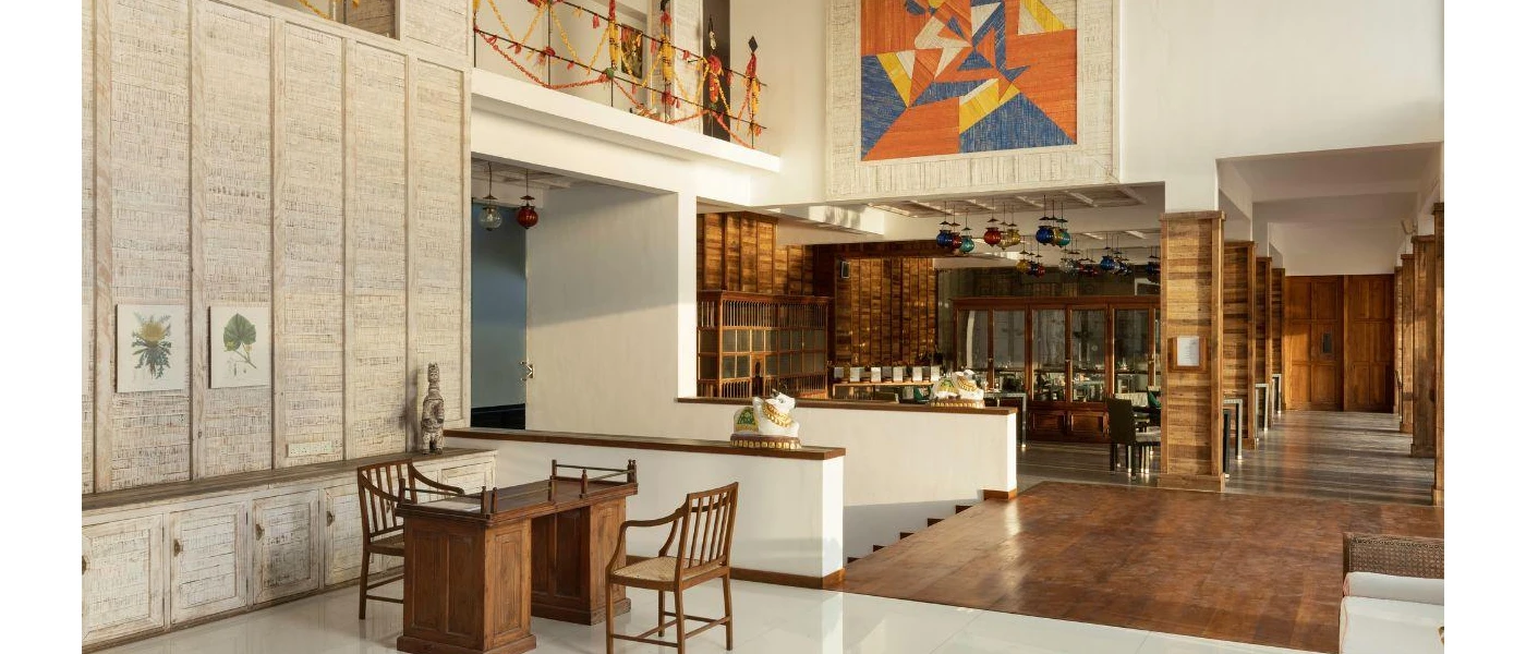 Hotel interiors with dark-wood pillars and walls, statues, hanging lanterns in rainbow colours, and a book shelf filled with books