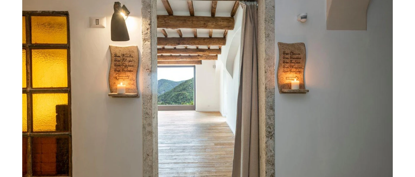 Entrance to a large light-filled room with a window overlooking green hills, with candles in scripture holders either side