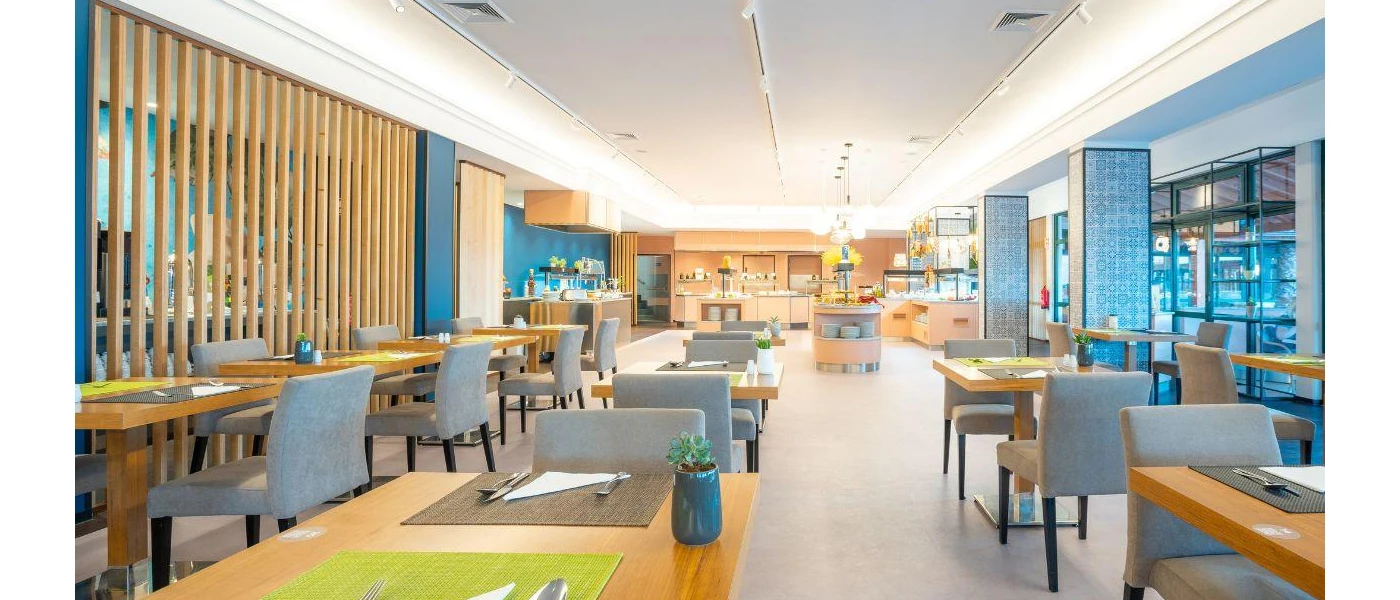 Bright restaurant with rows of grey chairs and wooden tables next to patterned columns 