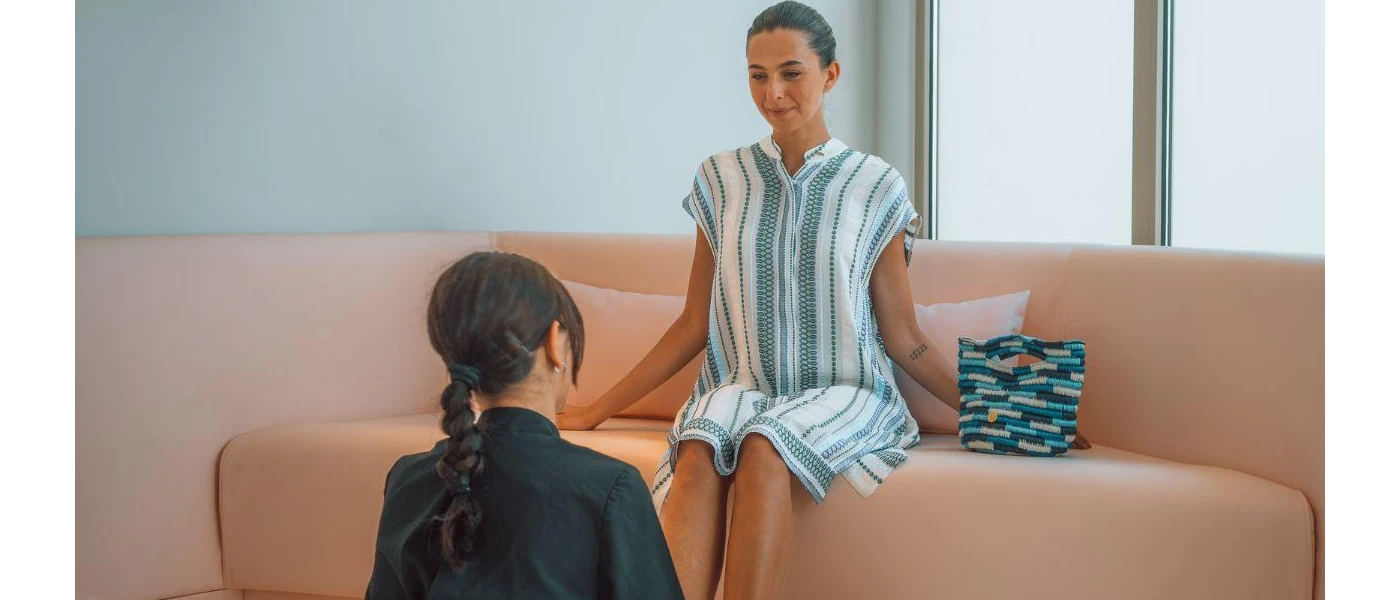 Woman in blue and white striped tunic sits on a sofa as a therapist sits at her feet