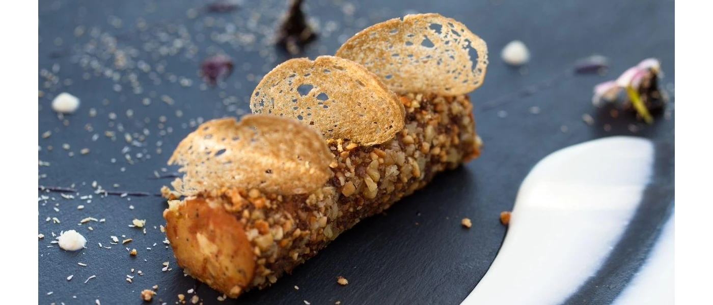 Intricately presented rolled food with breaded croutons on a black plate