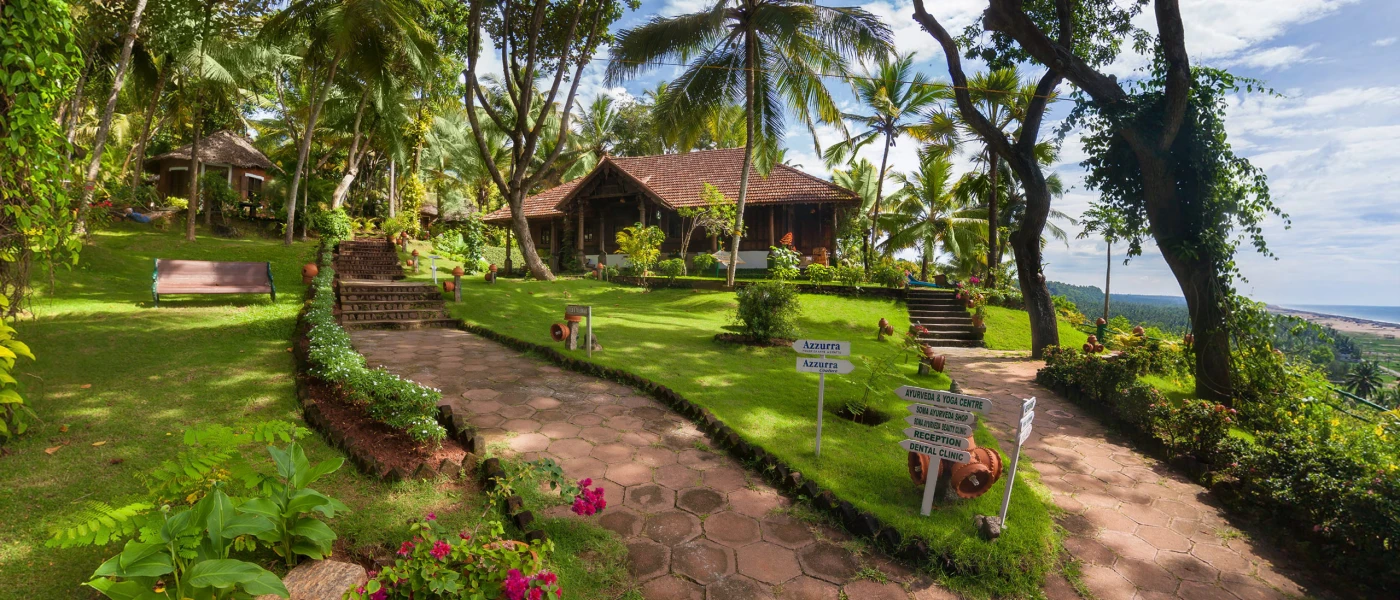 Traditional Indian buildings spread among lawns, pathways and coconut palms with the ocean in the background