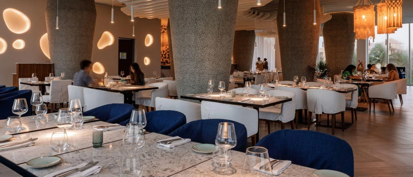 Modern restaurant with blue and grey chairs, marble-like tables, and macrame light lanterns