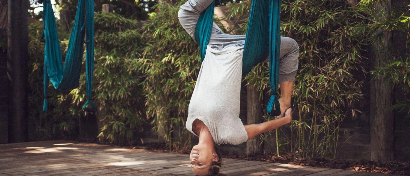 Woman hanging from a blue ribbon harness in a garden courtyard