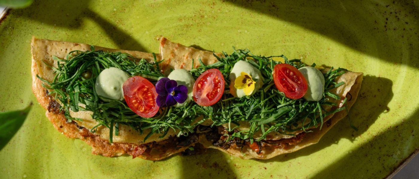 Crispy tacos folded over and topped with greens, tomatoes and edible pansies