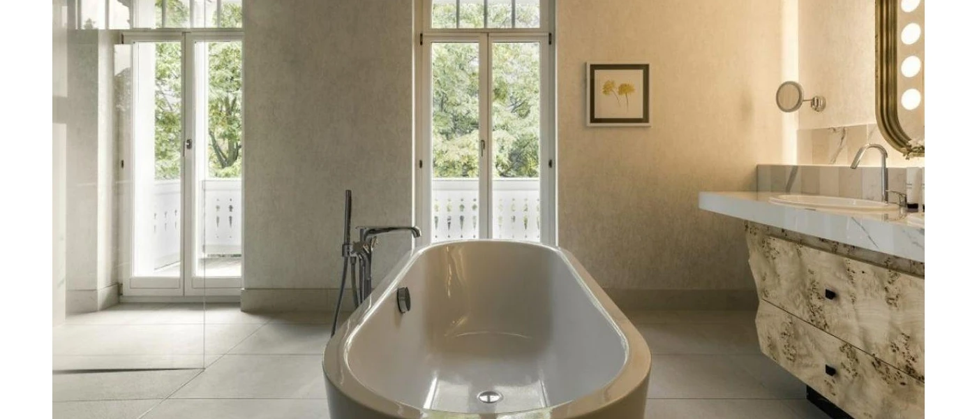Marble bathroom with freestanding bath, mirror with light bulbs surrounding it and floor-to-ceiling windows