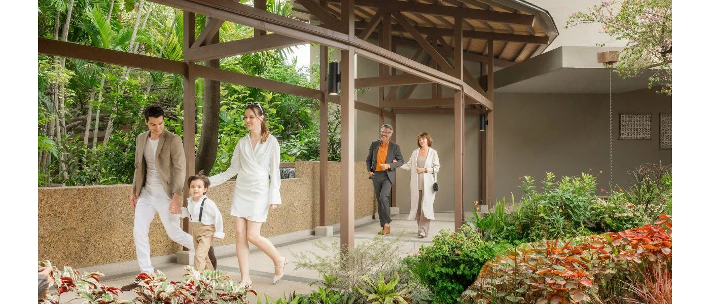 Man and woman with a child and a couple behind walk through a walkway surrounded by tropical plants