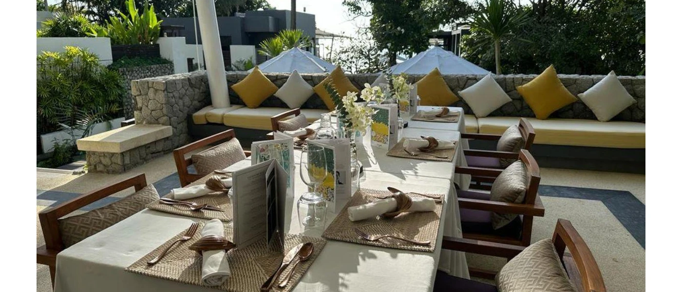 Stylish al fresco restaurant terrace with cobbled walls, yellow cushions and seat pillows, surrounding gardens and white umbrellas