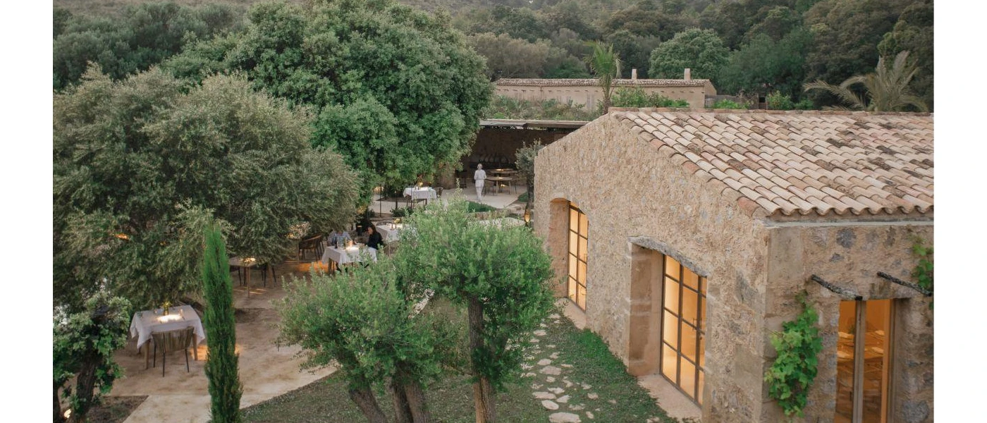 Traditional stone building surrounded by trees, and tables with white tablecloths set up for dining 