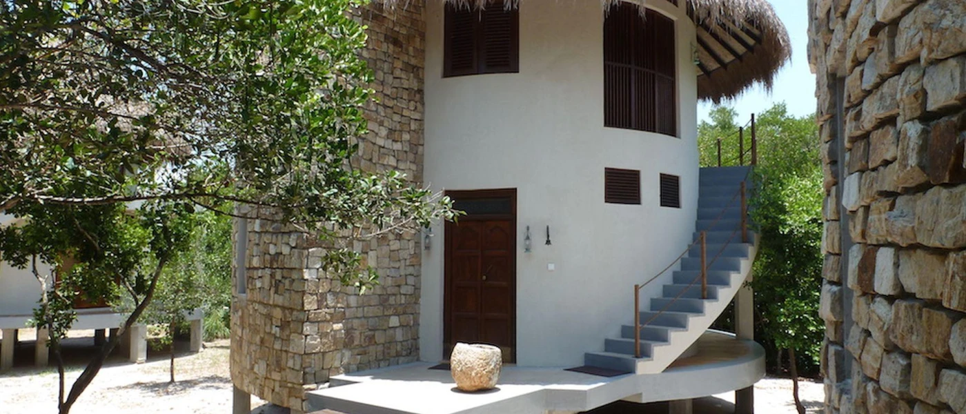 White circular building with stairs and a thatched triangular roof