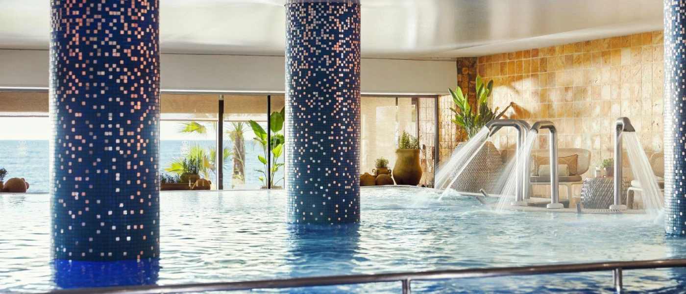 Indoor pool with blue tiled pillars and high-pressure water jets in a room with huge windows and sea views