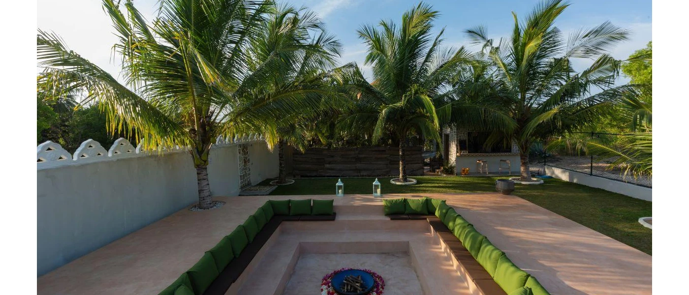 Lowered communal seating area, with green cushions and a central fire pit ringed by flowers