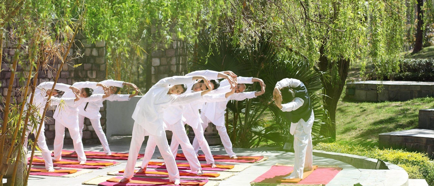 Group in white clothing stretching on yoga mats with an instructor, surrounded by tropical greenery