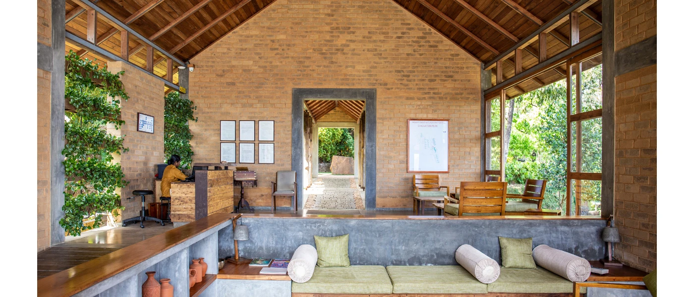 Cosy sofa area with neutral cushions in an airy room with a high wood-beamed ceiling, stone walls and foliage