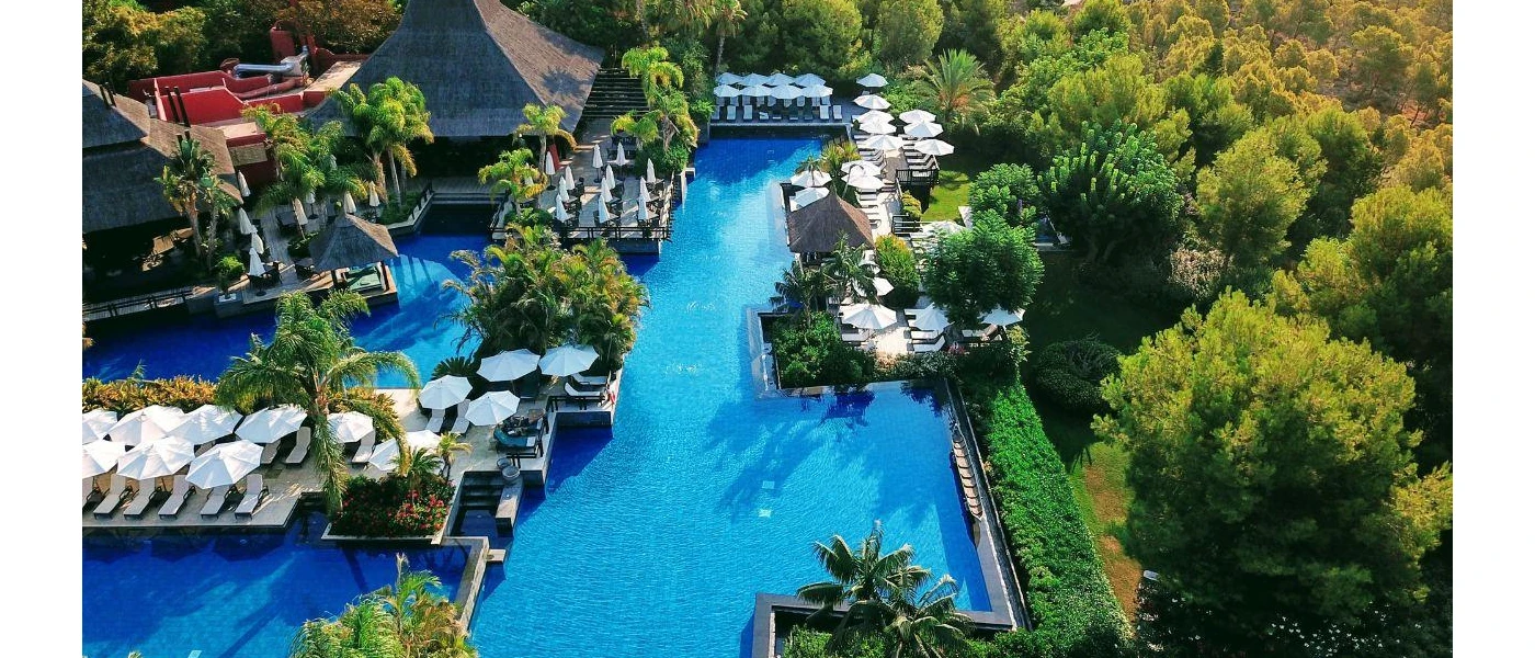 Lake-like pools surrounded by tropical greenery, white loungers and parasols and thatched-roof buildings