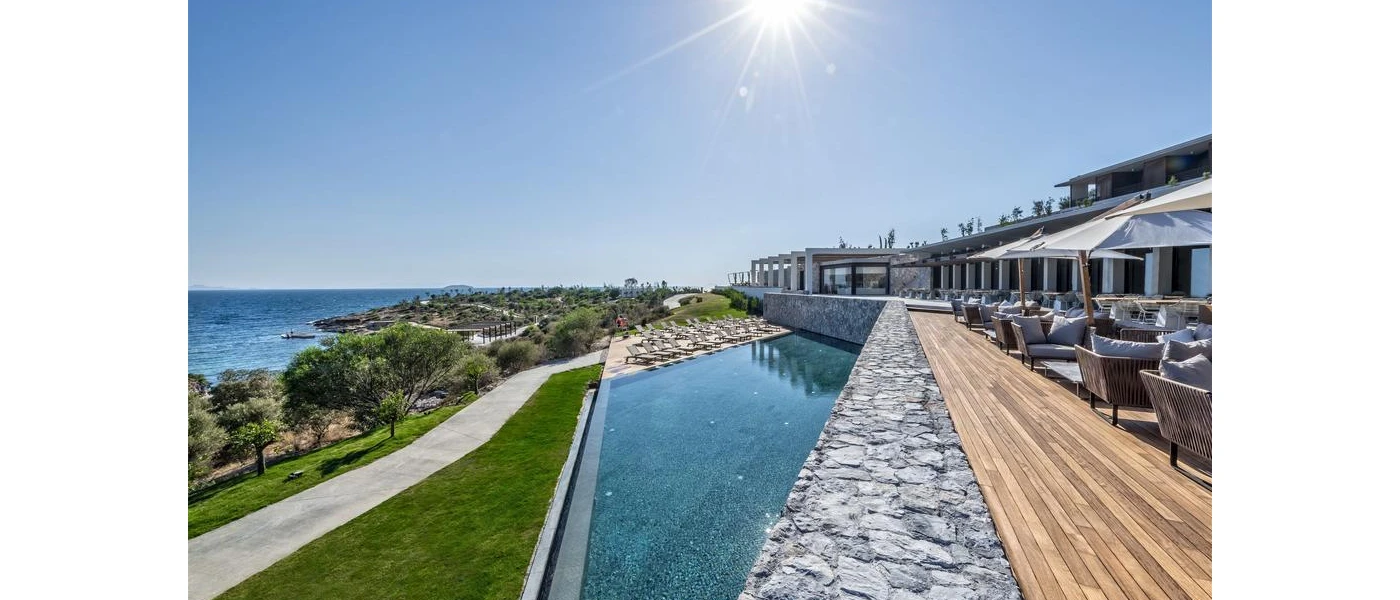 Outdoor pool and wooden terrace with tables, chairs and parasols, overlooking landscapes grounds and the Aegean Sea