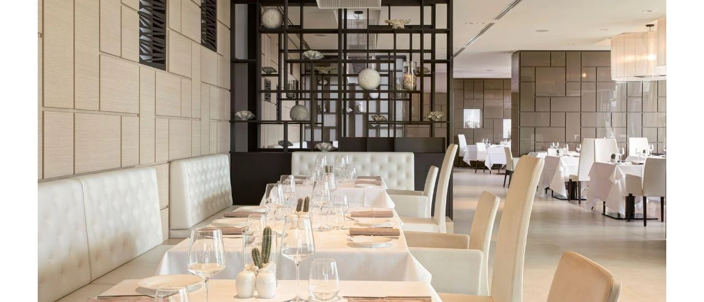 Airy restaurant with glossy tiled walls, dark-wood shelves stacked with ornaments, and white tablecloths