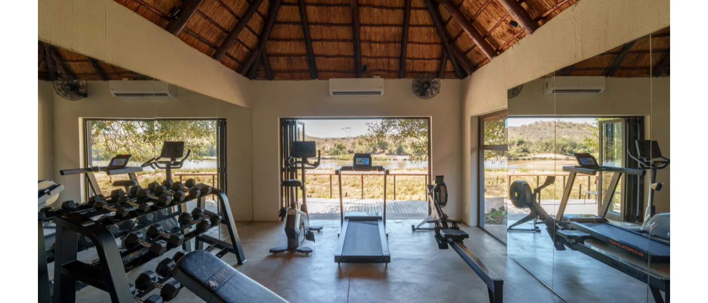 Gym with a wood-beamed ceiling and floor-to-ceiling windows, equipped with treadmills, benches, bikes and weights