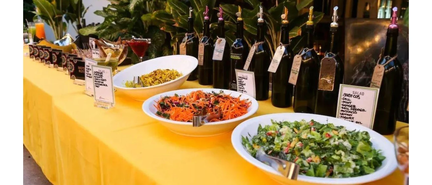 Bowls of salads and juices lined up on a long table with a yellow table cloth