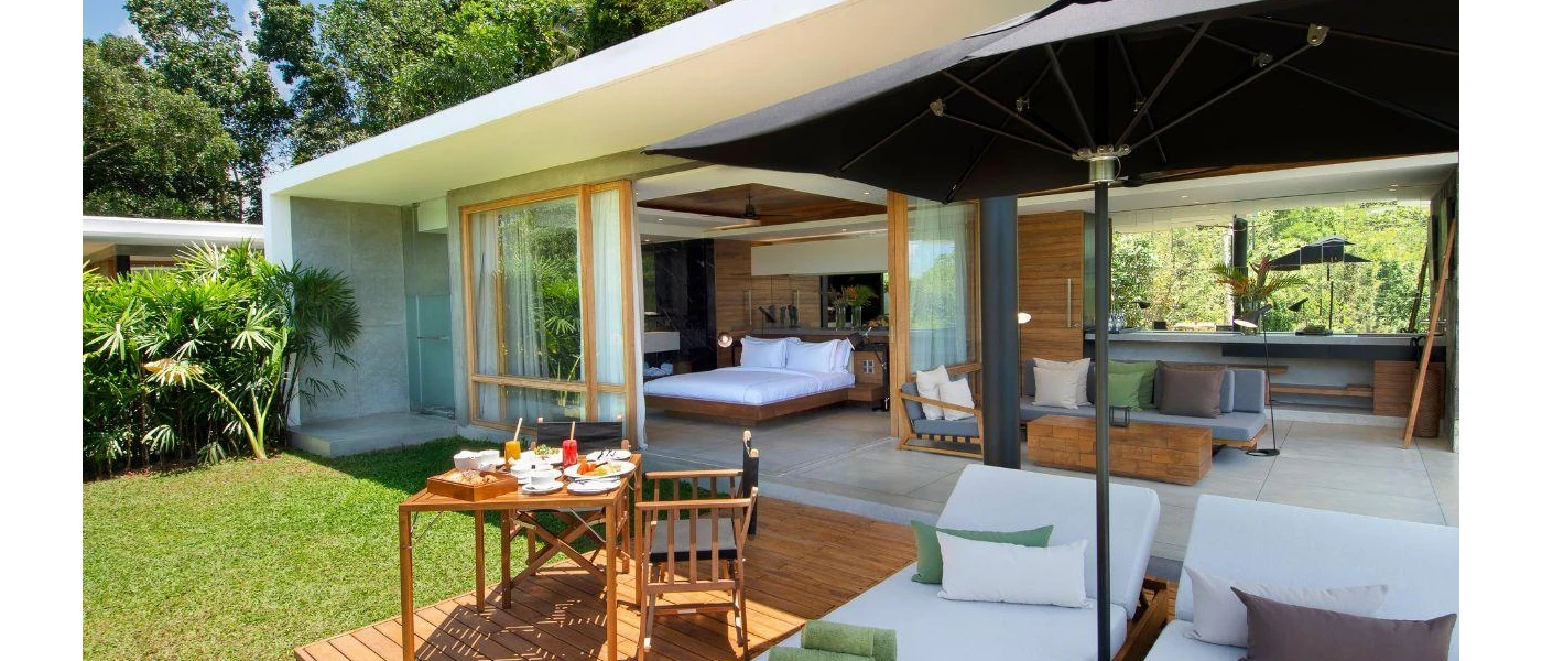 Villa with wooden furnishings, a bed overlooking the jungle and an outdoor terrace with a table and chairs and white cushioned loungers