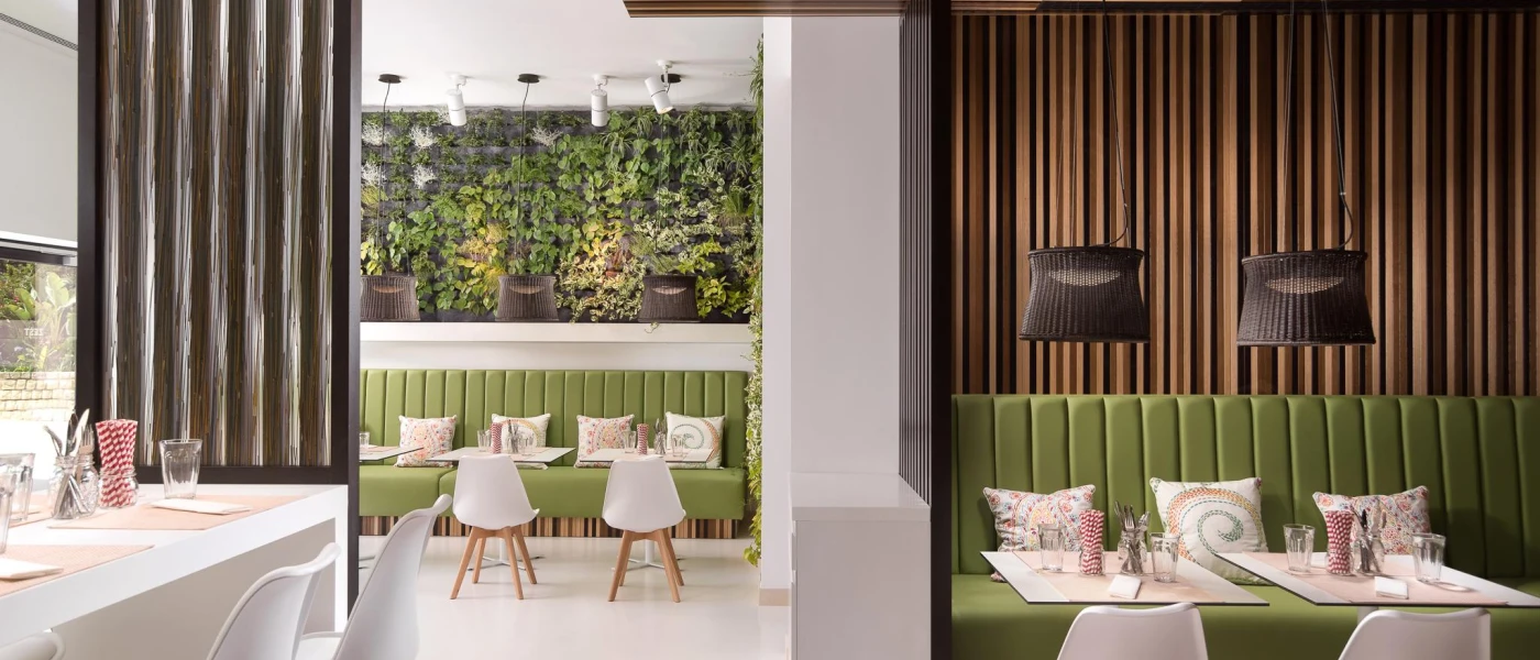 Stylish restaurant with wood-panelled walls, green sofa seating and a wall dressed in foliage