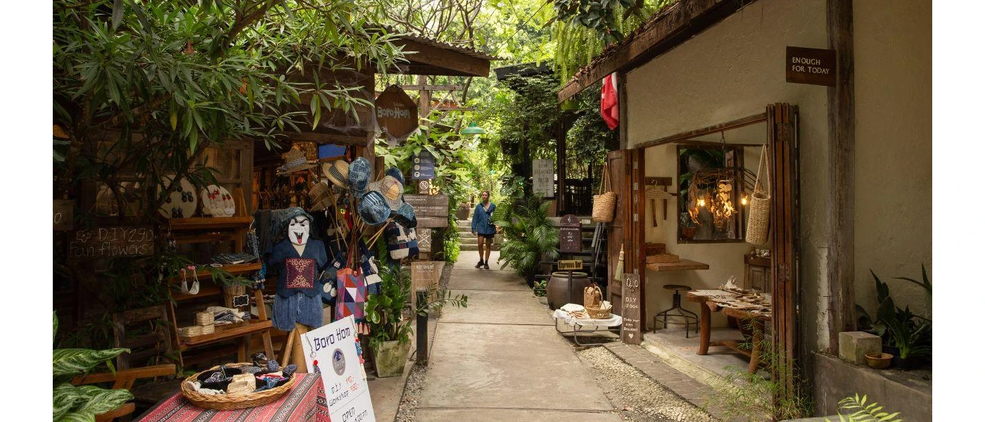 Woman walks down a tropical pathway with two stores selling handwoven baskets, hats and resort wear