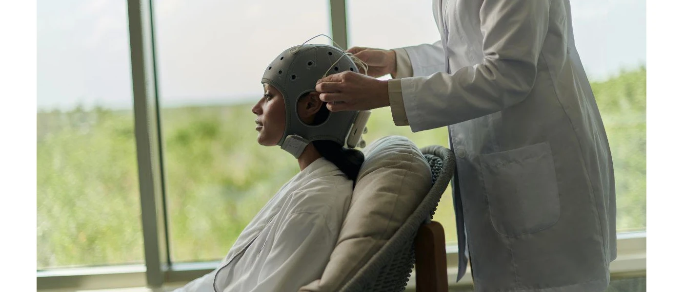 A woman sits in a chair as a therapist in a white coat fits an apparatus with tubes over her head