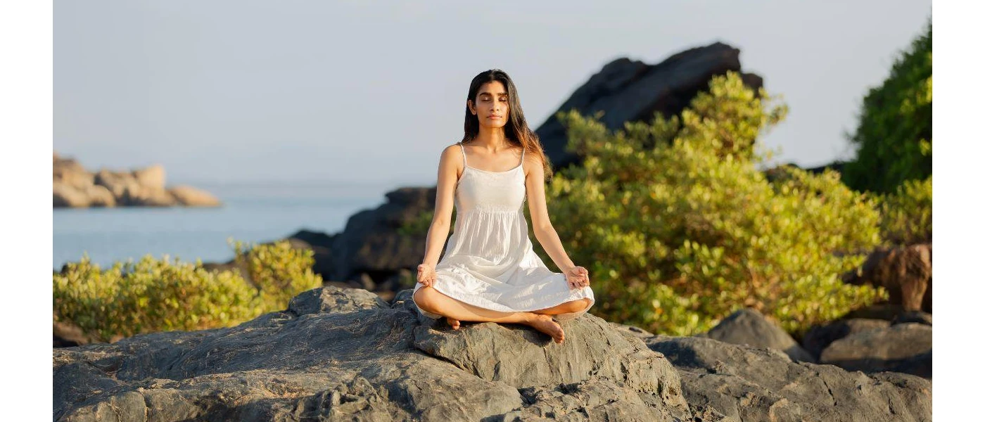Woman sitting by the ocean practising meditation on rocks