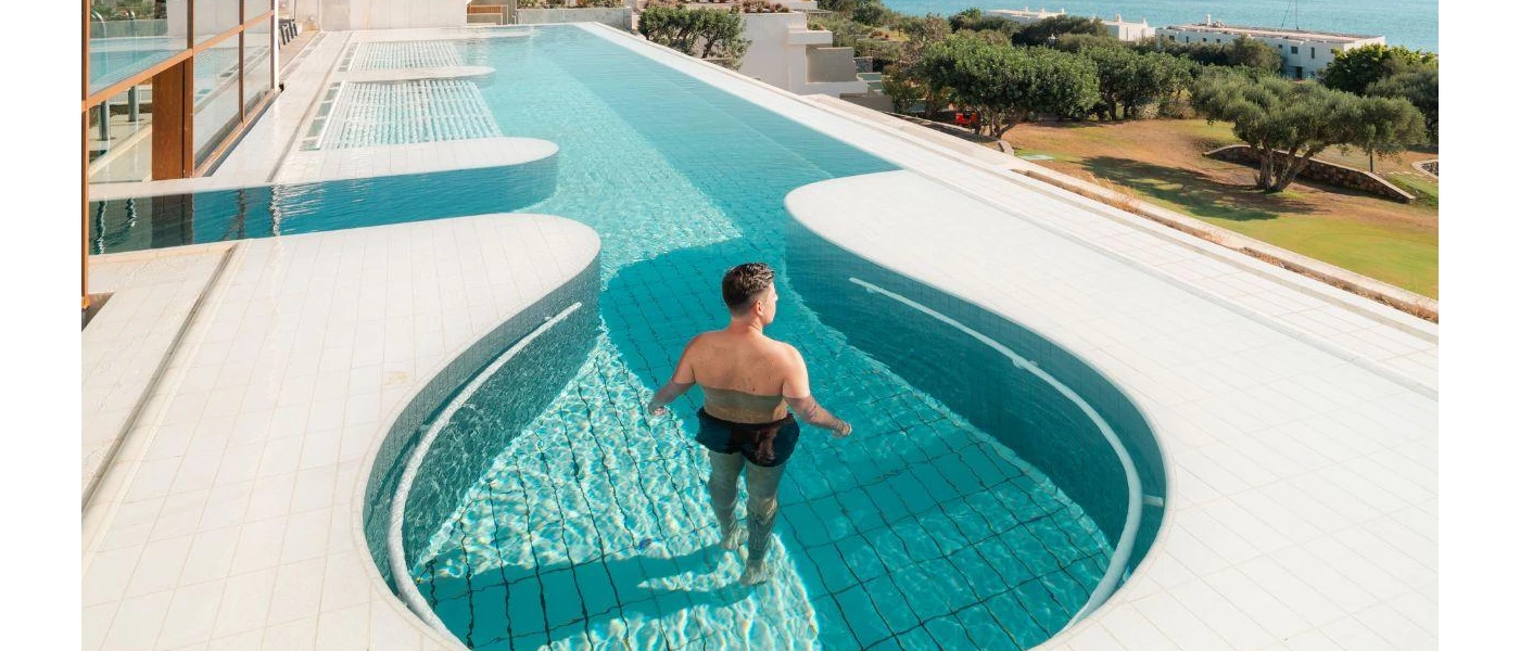 Man relaxes in a curvy pool set in a sunny terrace with views of the gardens and sea