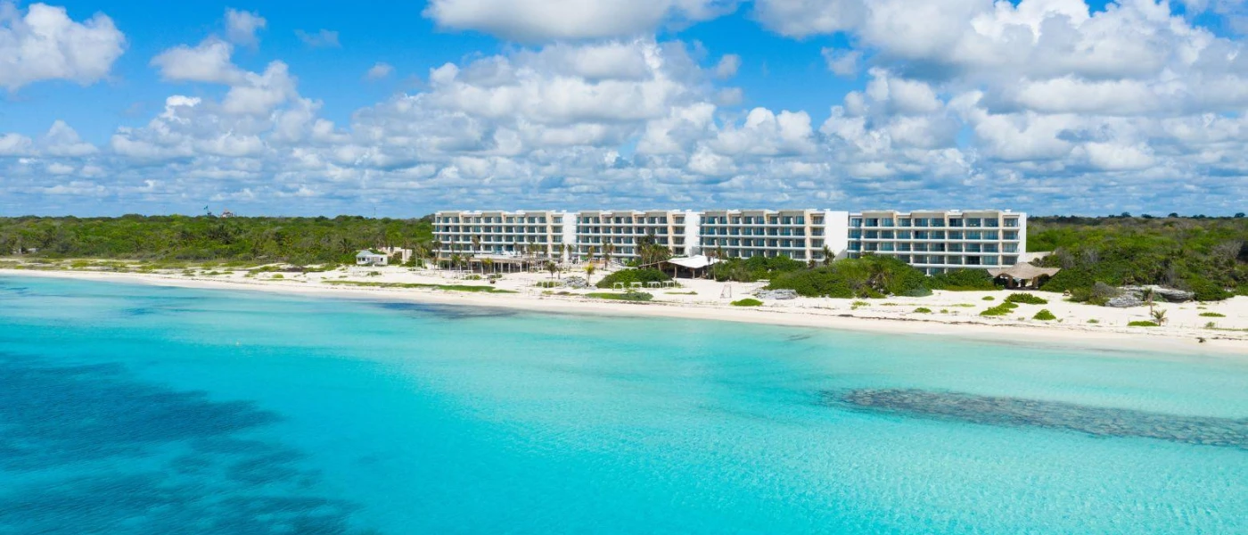 Vivid turquoise sea, white sand and high-rise white resort under a blue and white cloud sky