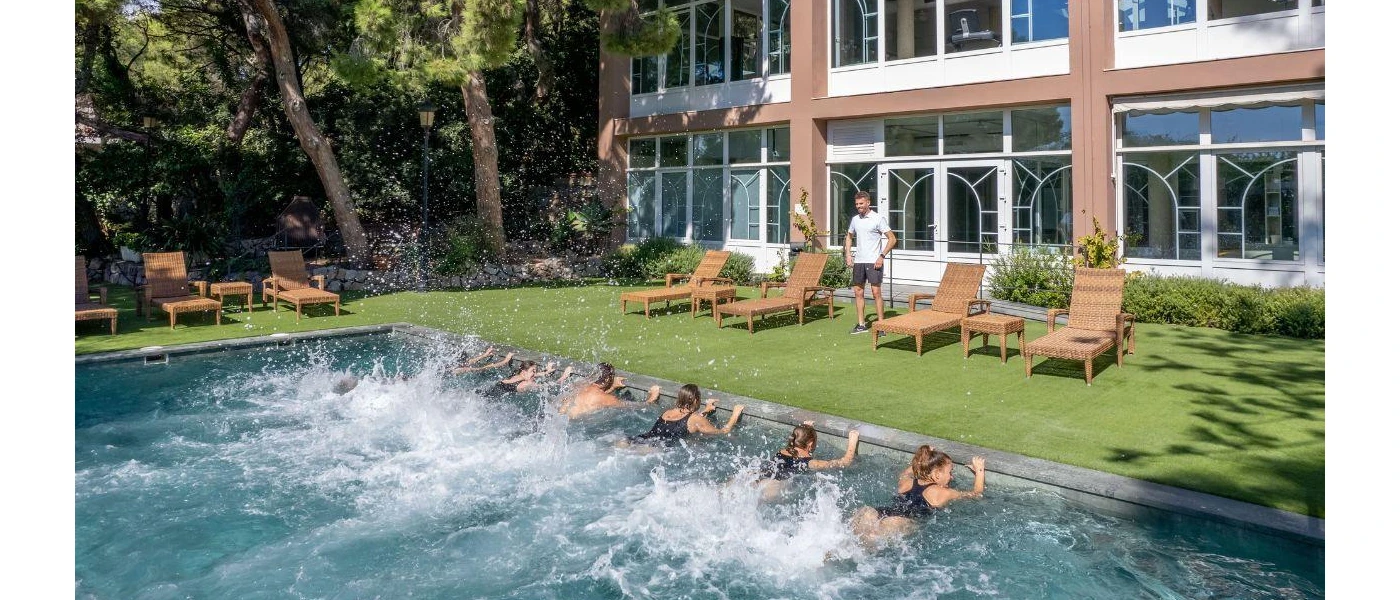 Group in black swimwear hold onto the side of a pool and kick their legs as part of a group class