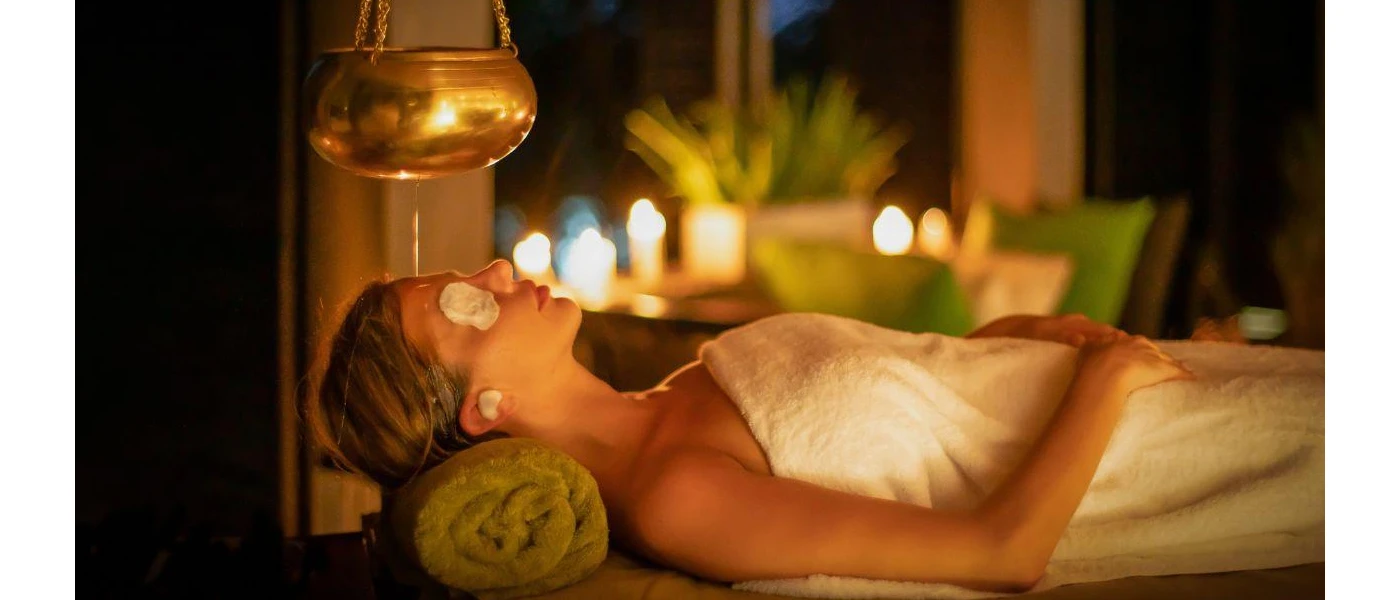 Woman relaxing in a towel on a massage bed with eye pads on and candles surrounding her
