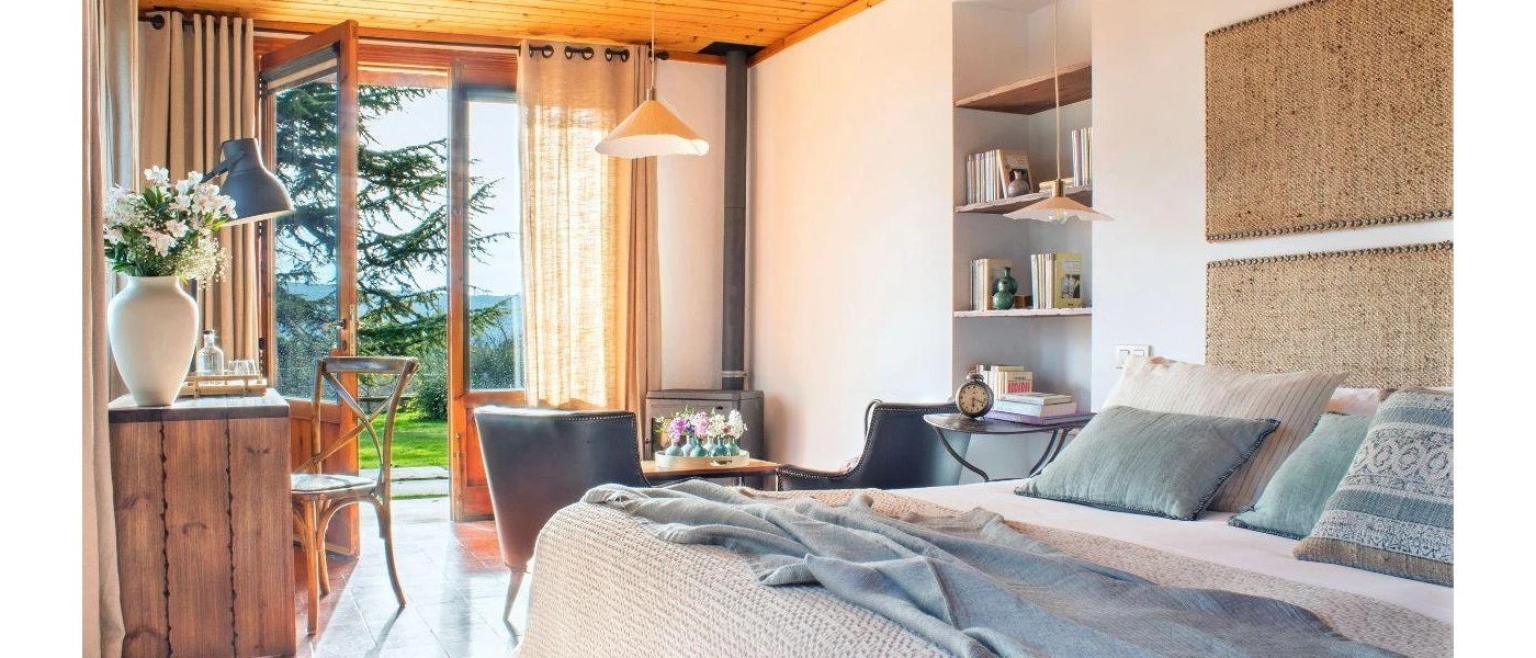 Farmhouse room with white walls, dark-wood furniture, wooden flooring and ceiling, and an open balcony door overlooking a garden